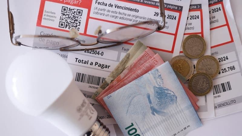 Chilean pesos, coins, utility bills, and a light bulb representing rising household costs and inflation.