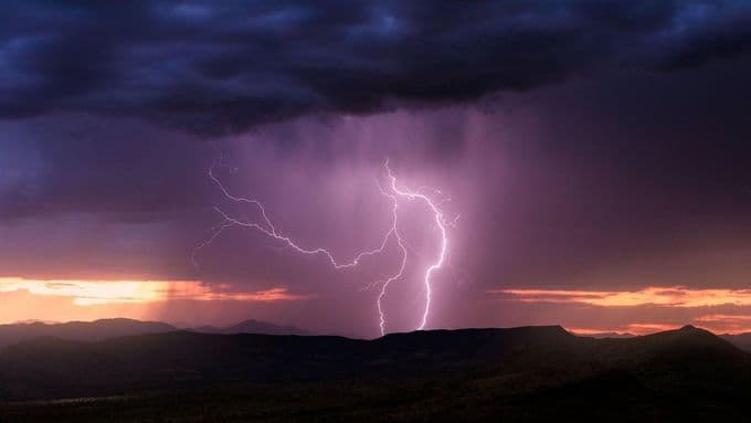 Éclair frappant le sol sous un ciel d'orage sombre au-dessus de montagnes, illustrant les prévisions du CHMÚ face aux orages estivaux.