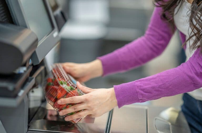 Client scannant une barquette de fraises à la caisse automatique de supermarché.