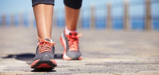 Close-up of a person's feet in running shoes walking on pavement, symbolizing outdoor activity precautions during a heatwave.