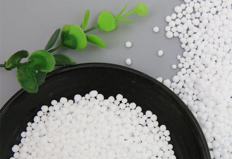 Close-up of white urea fertilizer granules in a bowl alongside decorative greenery.
