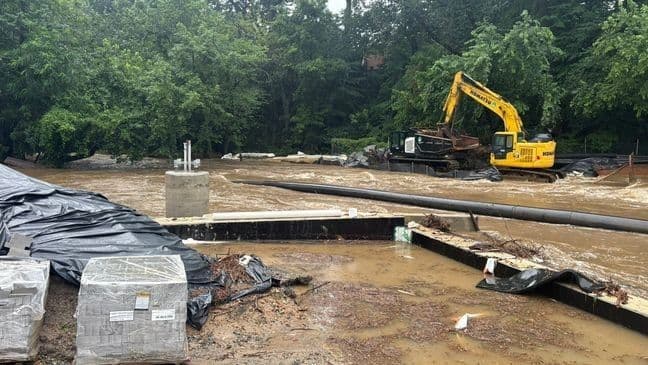 Construction equipment and materials are visible next to a muddy, debris-filled waterway, representing infrastructure improvements and resilience efforts against flooding.