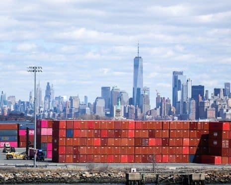 Conteneurs maritimes au port de New York avec la skyline de Manhattan, représentant le commerce international et les tarifs douaniers.