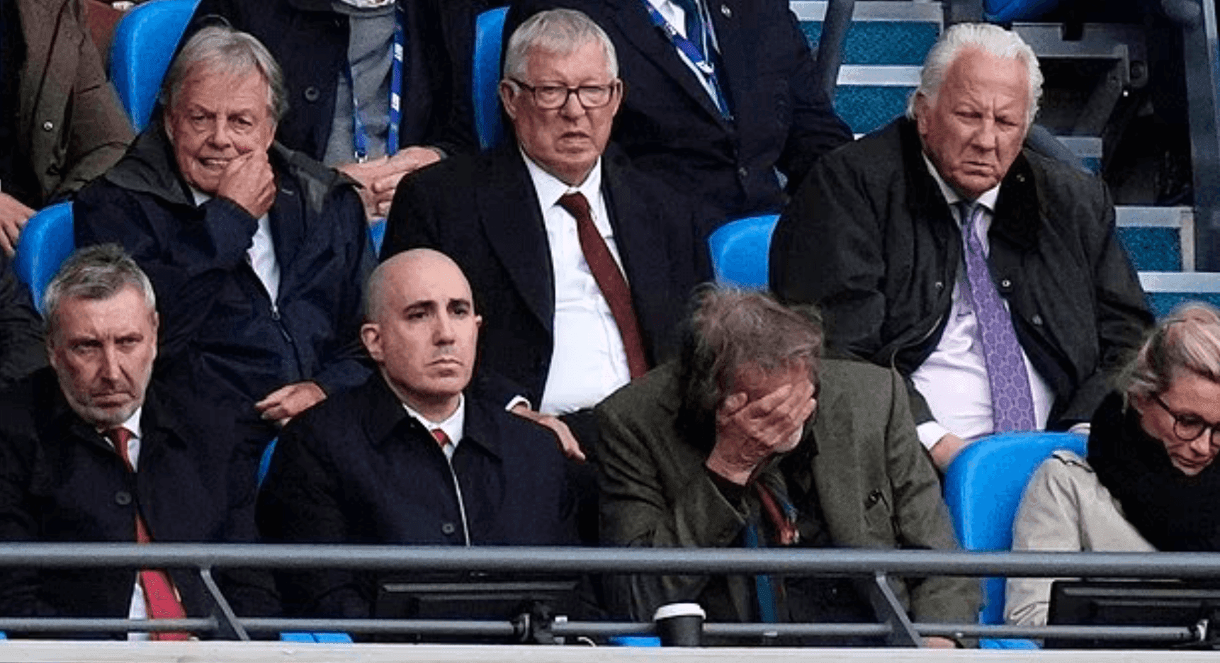 Dejected Manchester United fans, including Sir Alex Ferguson, reacting to the team's poor performance.