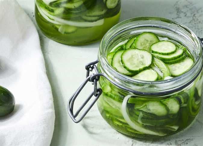 Des concombres et oignons tranchés en saumure dans des bocaux, illustrant l'audace culinaire et les techniques de transformation des légumes.