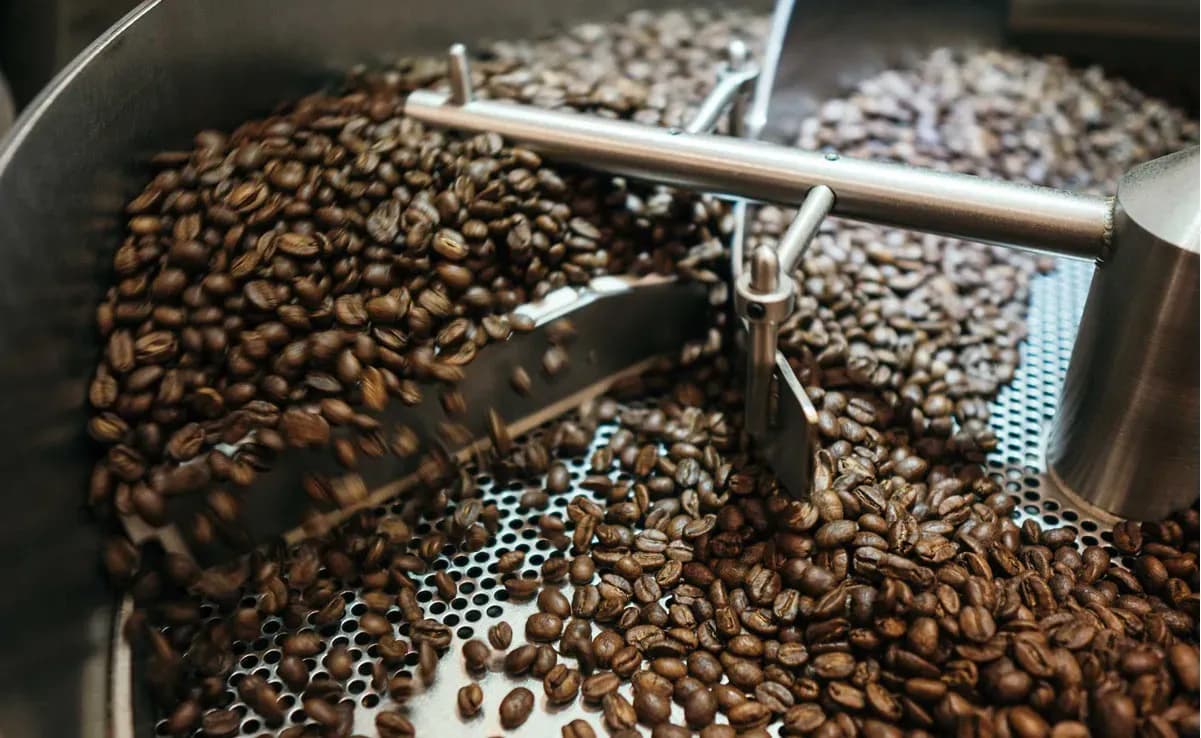 Des grains de café torréfiés dans une machine, symbolisant la transformation et le marché du café en ligne.