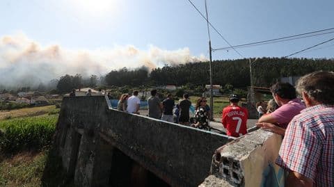 Des habitants de Ponteceso observent impuissants la fumée d'un incendie de forêt s'élevant au-dessus des collines.