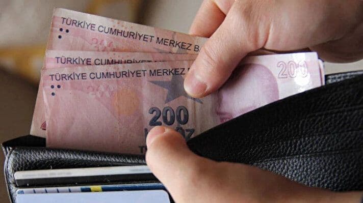 Des mains plaçant des billets de lire turque dans un portefeuille, symbolisant la gestion des dépenses et l'impact financier.