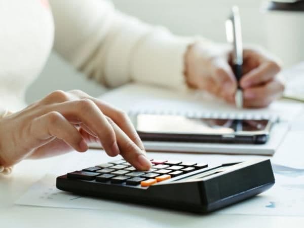Des mains utilisant une calculatrice et écrivant, illustrant le processus de déclaration de revenus pour les millions de contribuables.