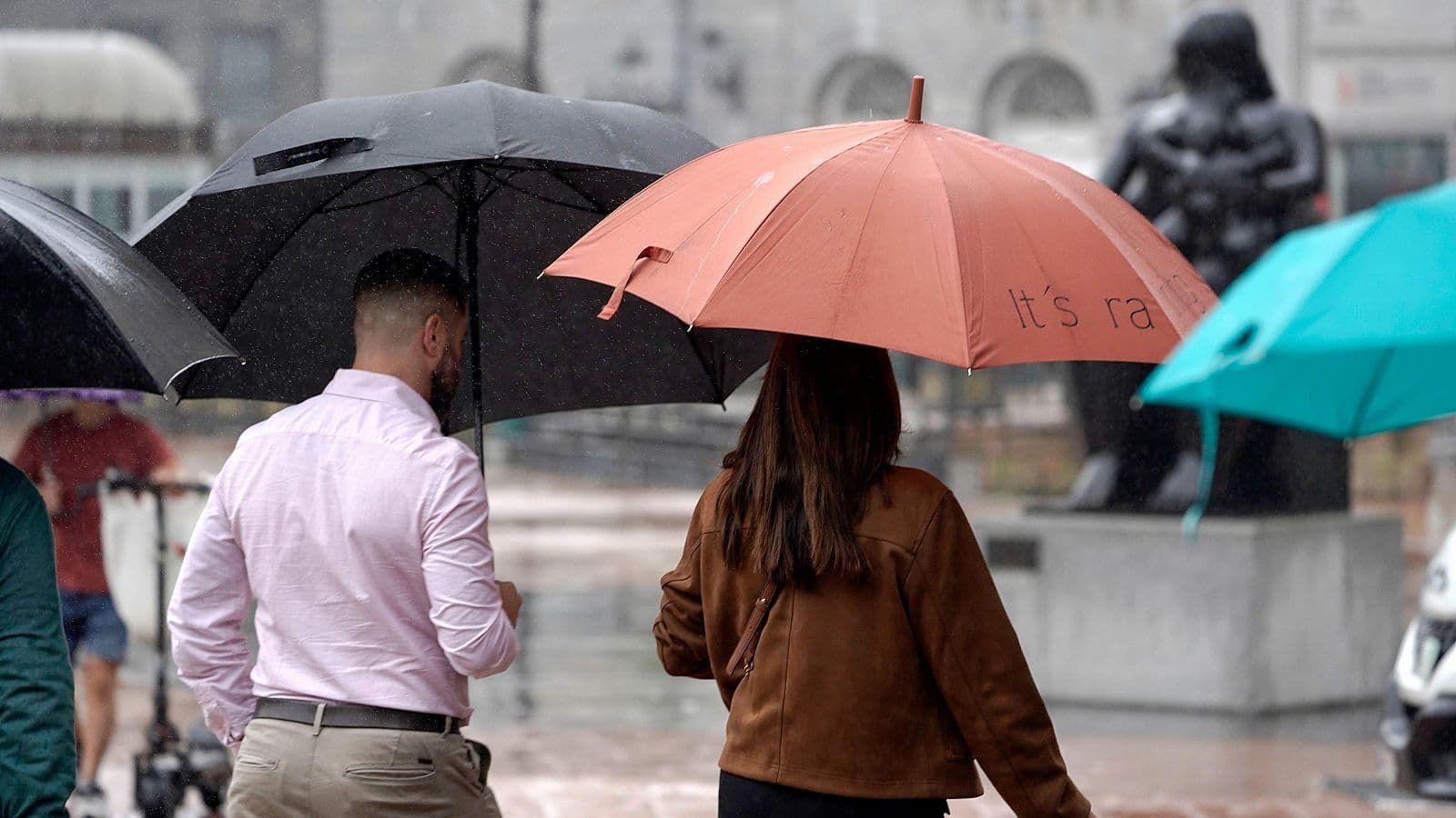 Des personnes avec des parapluies sous la pluie en Espagne, illustrant le contraste météorologique de l'été.