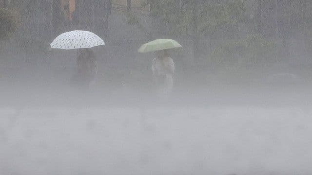 Des personnes marchant sous de fortes pluies avec des parapluies, illustrant l'impact des conditions météorologiques extrêmes sur le quotidien.