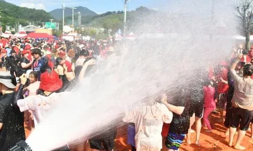 Des personnes se rafraîchissent sous un jet d'eau tandis que des pluies extrêmes et des orages sont annoncés, symbolisant l'alternance entre canicule et déluge en Corée du Sud.