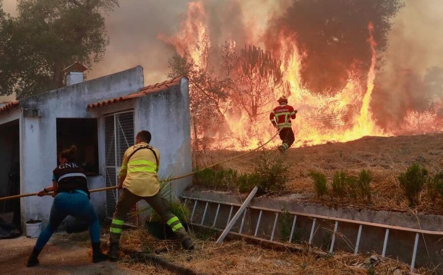 Des pompiers portugais combattant un violent incendie de forêt près d'une maison, illustrant le déploiement d'urgence.
