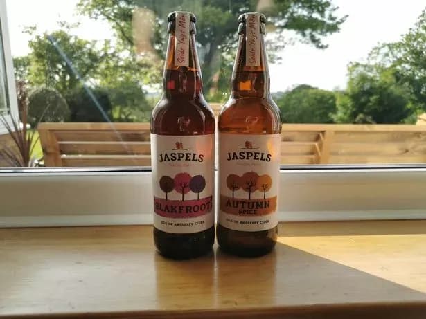 Deux bouteilles de cidre artisanal Jaspels, l'une 'Blakfroot' et l'autre 'Autumn Spice', sur un rebord de fenêtre.