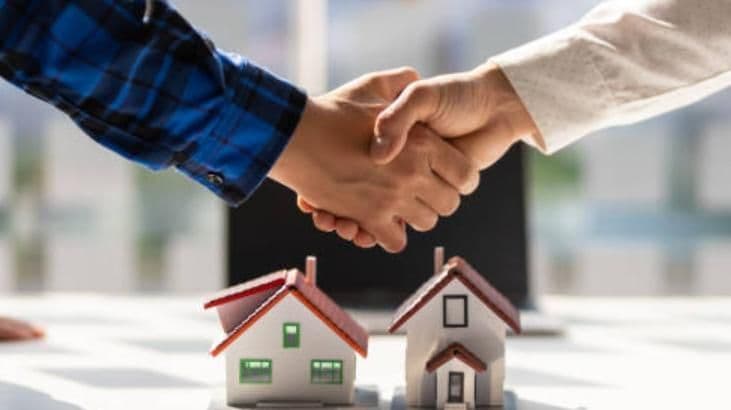 Deux personnes se serrant la main au-dessus de maquettes de maisons, représentant les transactions et l'équilibre dans le secteur immobilier.