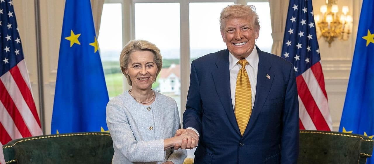 Donald Trump et Ursula von der Leyen se serrant la main devant les drapeaux des États-Unis et de l'Union européenne, symbolisant l'accord commercial.
