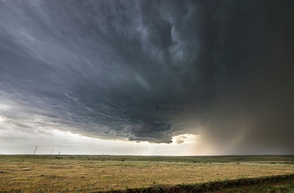 Dramatic dark storm clouds gathering over a flat landscape with heavy rain falling in the distance, symbolizing a severe summer squall.