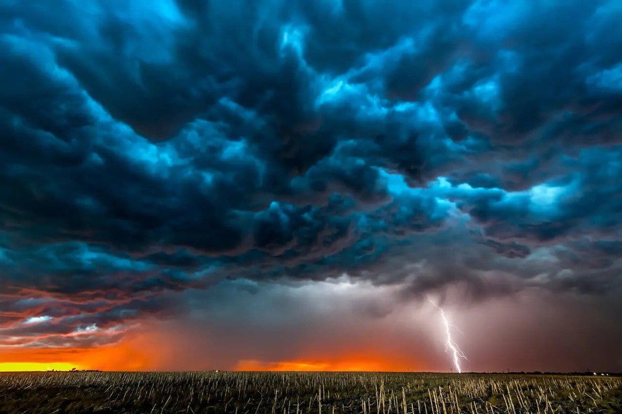 Dramatic dark storm clouds with lightning striking a field at sunset, symbolizing the arrival of a powerful cold front.