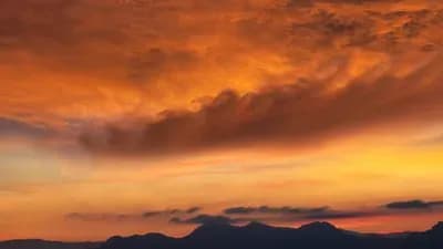 Dramatic orange and red clouds over a mountain range, symbolizing the extreme and divided weather patterns in Kazakhstan.
