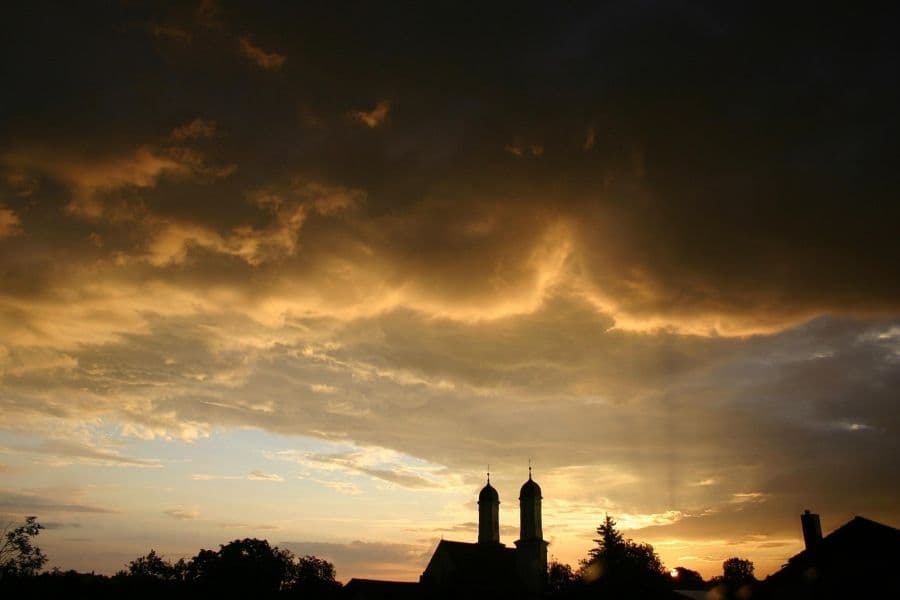 Dramatic stormy clouds at sunset over a silhouetted church in Hungary, symbolizing August's dynamic summer skies.