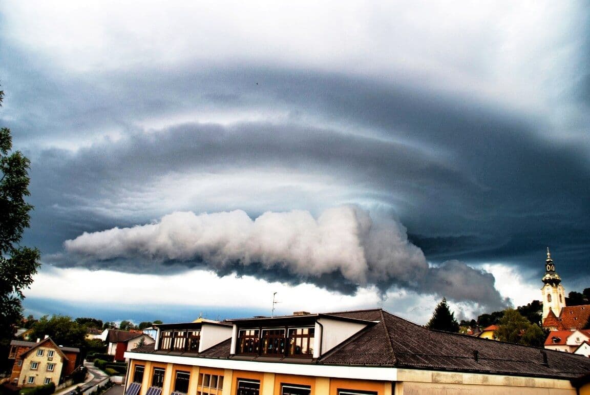 Dramatic supercell thunderstorm cloud formation over an Austrian town, signaling escalating hail threat.
