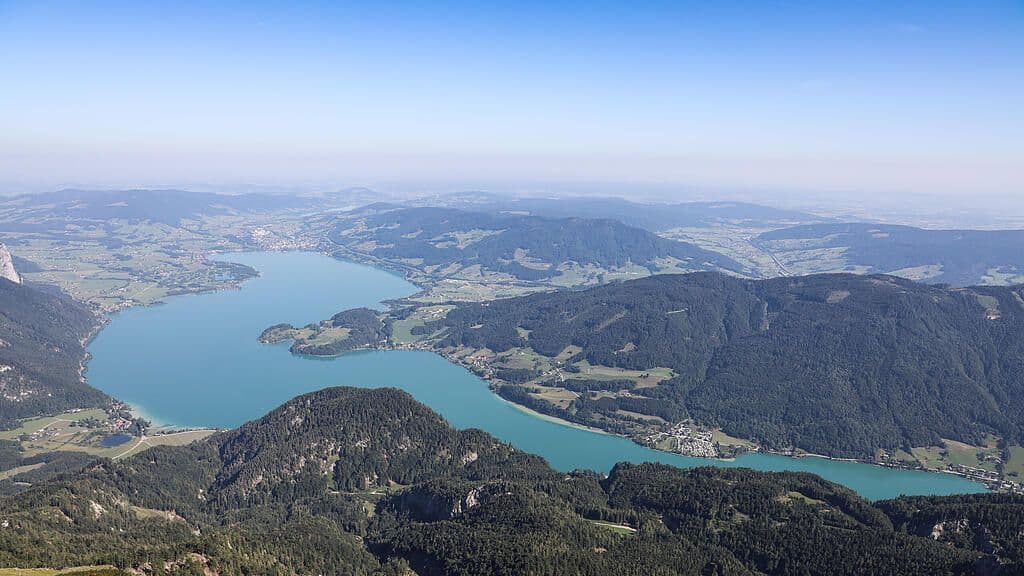 Expansive aerial view of Mondsee lake nestled among green alpine mountains under a clear sky