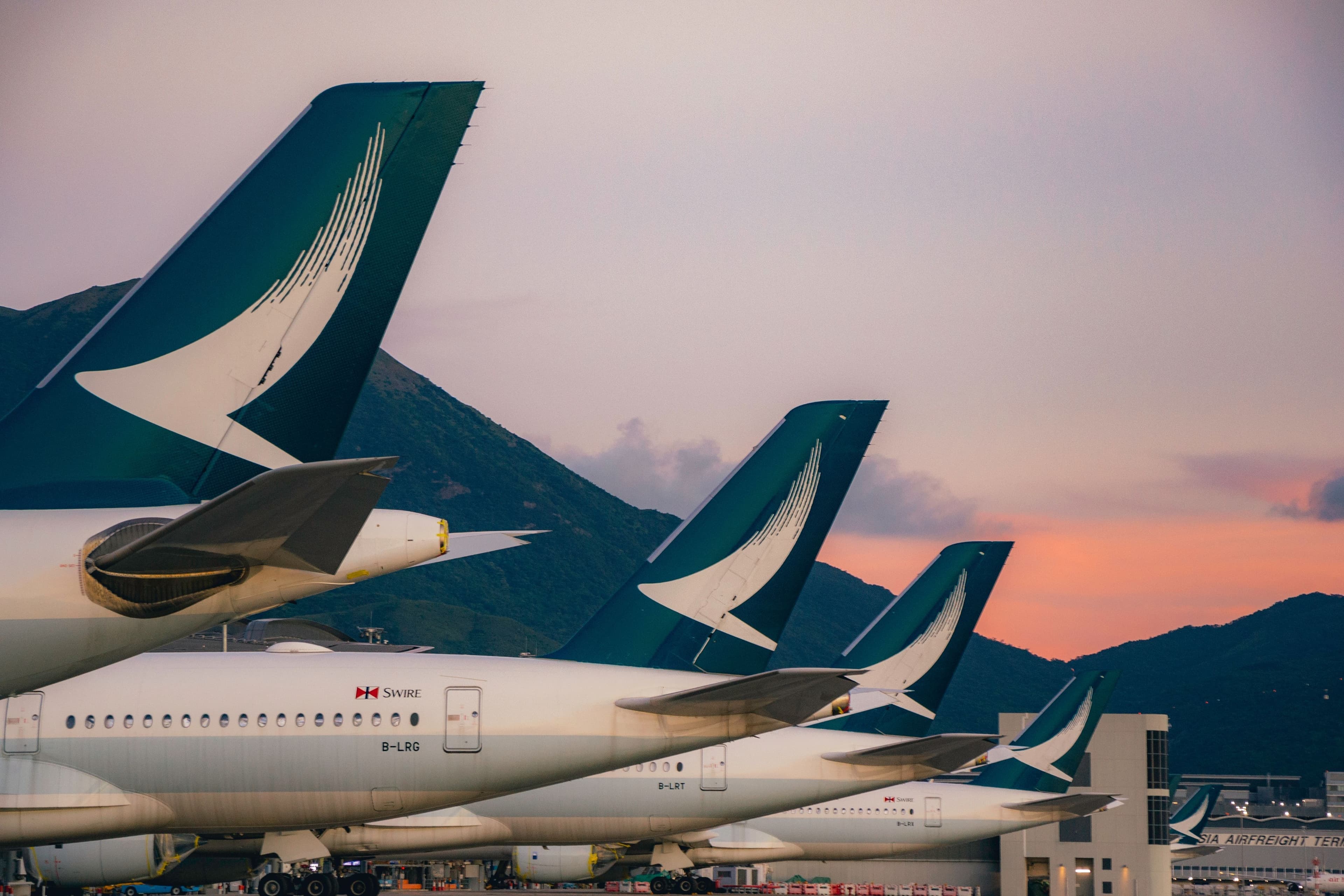 Flotte d'avions Cathay Pacific à l'aéroport de Hong Kong au lever ou coucher du soleil, symbolisant la vision d'un géant aérien réinventé.