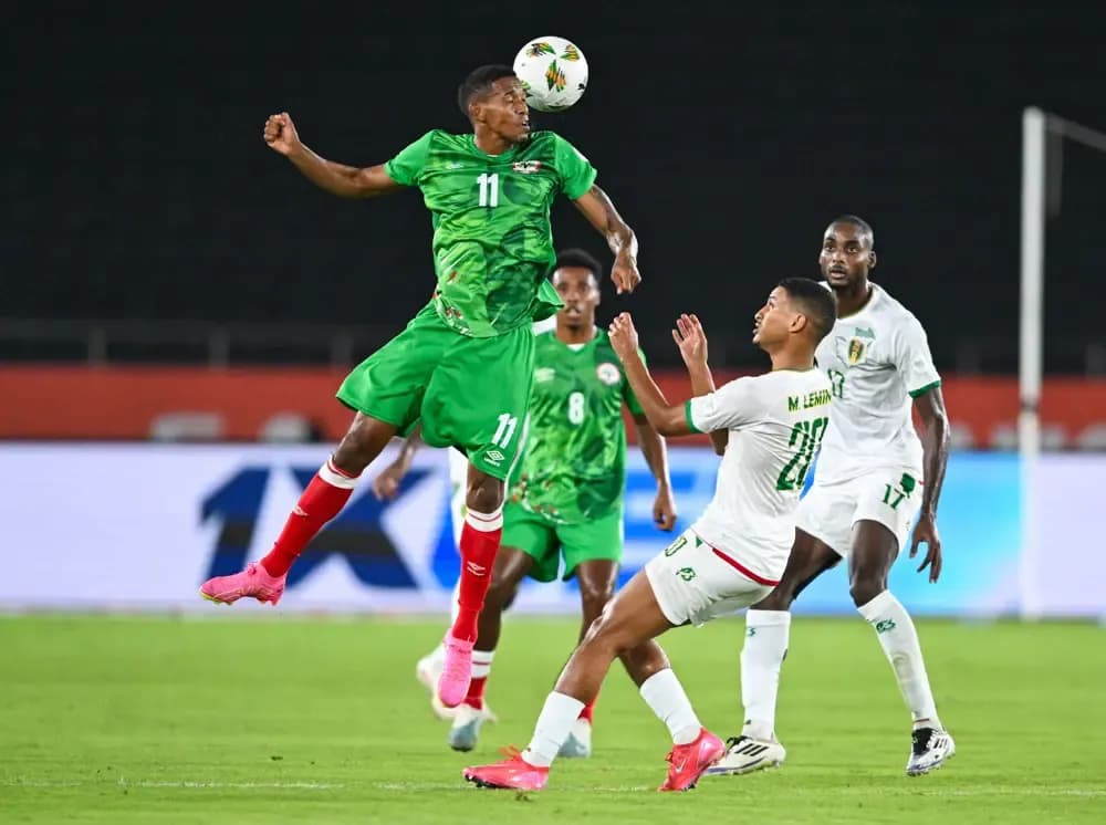Football players in green and white jerseys competing for the ball in mid-air during a CHAN 2025 match, showcasing local talent.