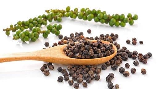 Grains de poivre vert sur la vigne et grains de poivre noir séchés, symbolisant la chaîne de valeur et la stabilité de la filière poivre.