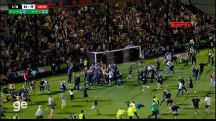Grimsby Town players and fans celebrating on the pitch after defeating Manchester United in a penalty shootout