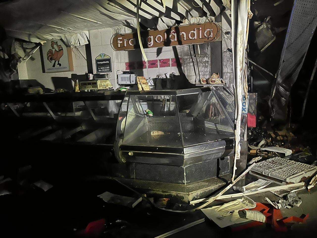 Interior de uma barraca do Mercado Municipal de Piracicaba após o incêndio, mostrando balcões e mercadorias carbonizadas.