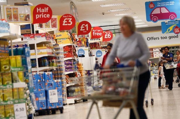 Interior view of a supermarket aisle with various products on shelves and 'Half price' signs, representing the retail environment.