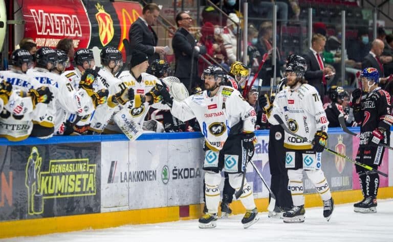 Jääkiekkoilijat vaihtopenkillä ottelun aikana, kuvastaen Mestiksen kiivasta kilpailua ja joukkueiden omia saavutuksia.