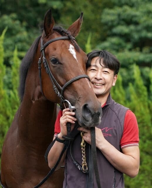 Keisuke Matsuzaki, a dedicated assistant trainer, smiling while embracing the champion racehorse Liberty Island.