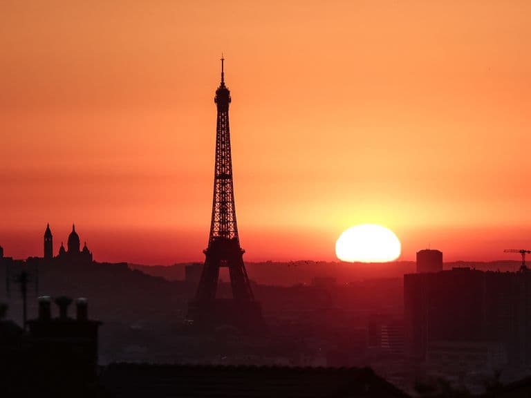 La Tour Eiffel se dresse sous un ciel orange vif au lever ou coucher du soleil, symbolisant la chaleur urbaine.
