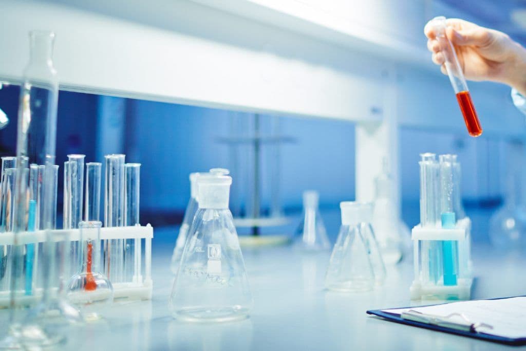 Laboratory equipment and a hand holding a test tube, symbolizing scientific investigation and diagnosis in response to Italy's botulism crisis.