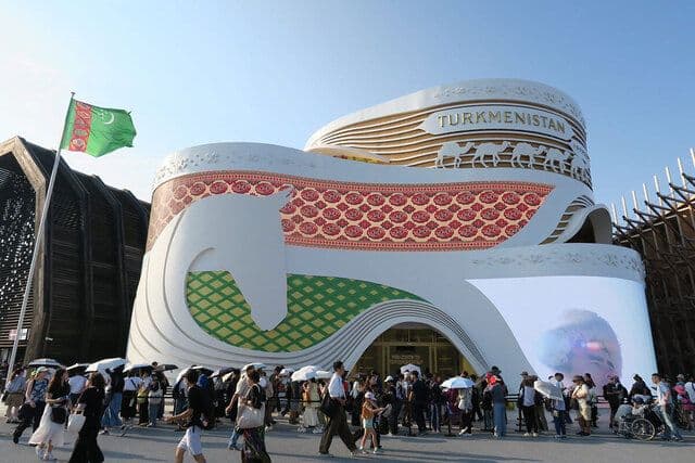 Le pavillon du Turkménistan à l'Expo 2025 d'Osaka, avec ses motifs de cheval et de chameaux, et le drapeau turkmène flottant.