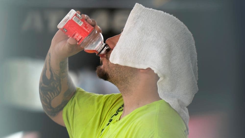 Man drinking water with a towel on his head, demonstrating strategies for staying safe in extreme heat.