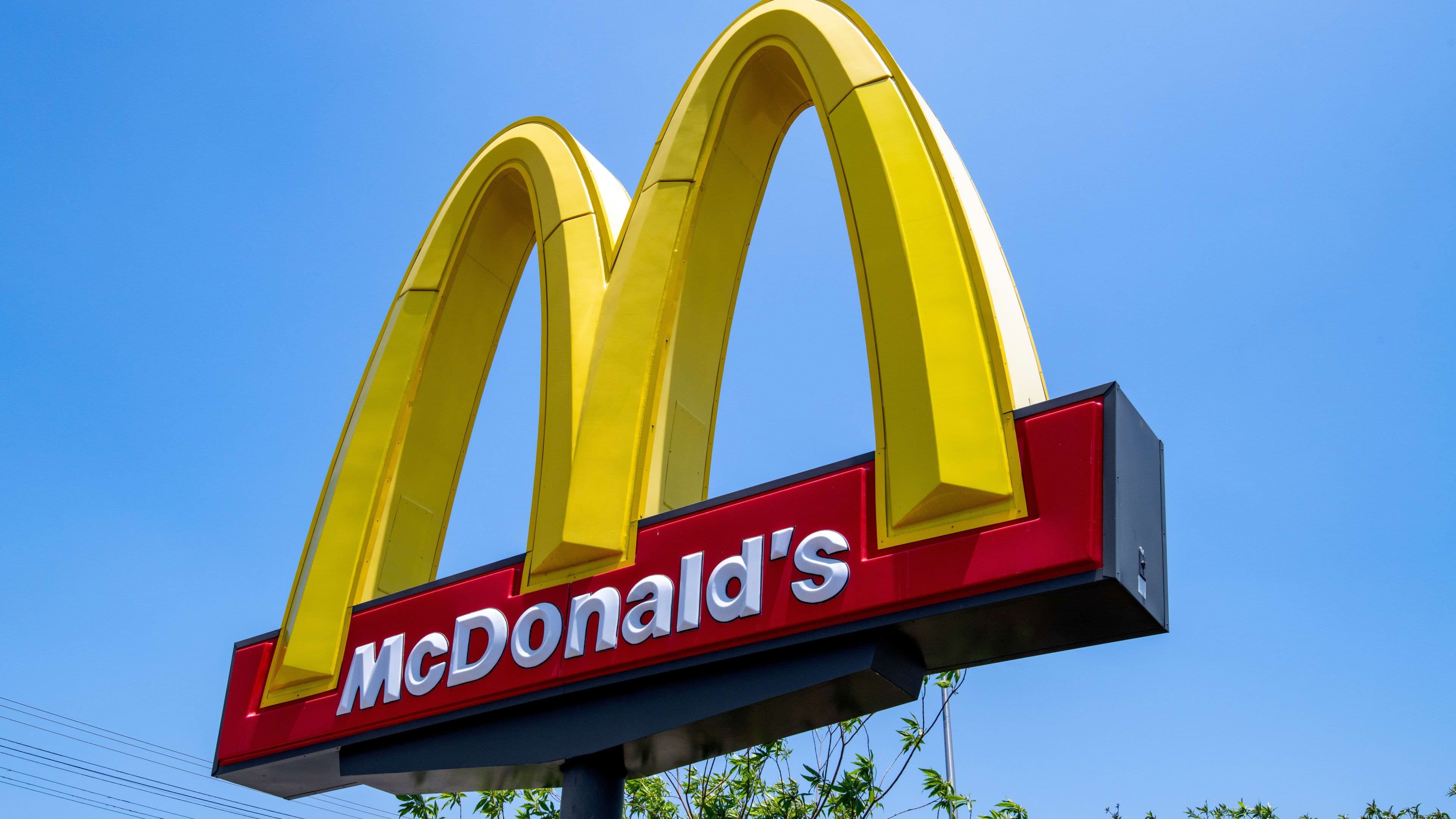 McDonald's golden arches sign against a clear blue sky, symbolizing the fast-food chain's presence.