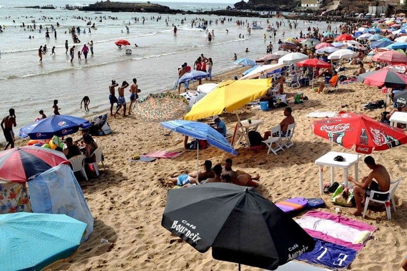 Moroccan beach crowded with people and umbrellas under a sunny sky, representing coastal climate and adaptation to heat.