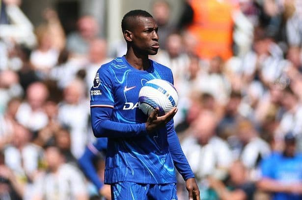 Nicolas Jackson, joueur de Chelsea, tenant un ballon de football avec une expression sérieuse, au milieu des tensions de son mercato.