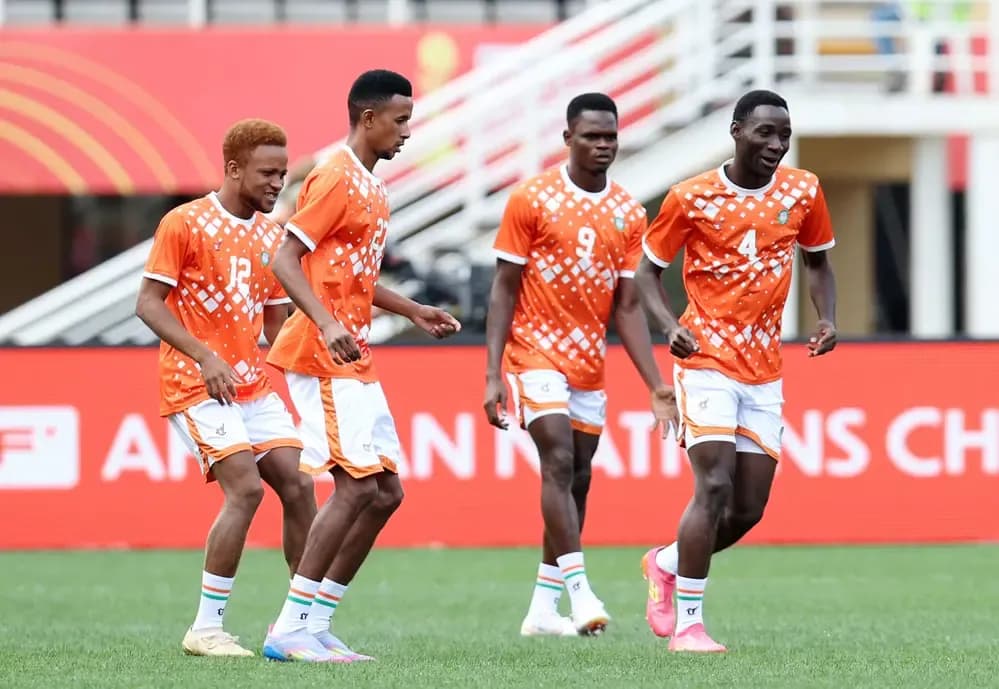 Nigerien football players in orange and white uniforms on the pitch, preparing for a high-stakes match.