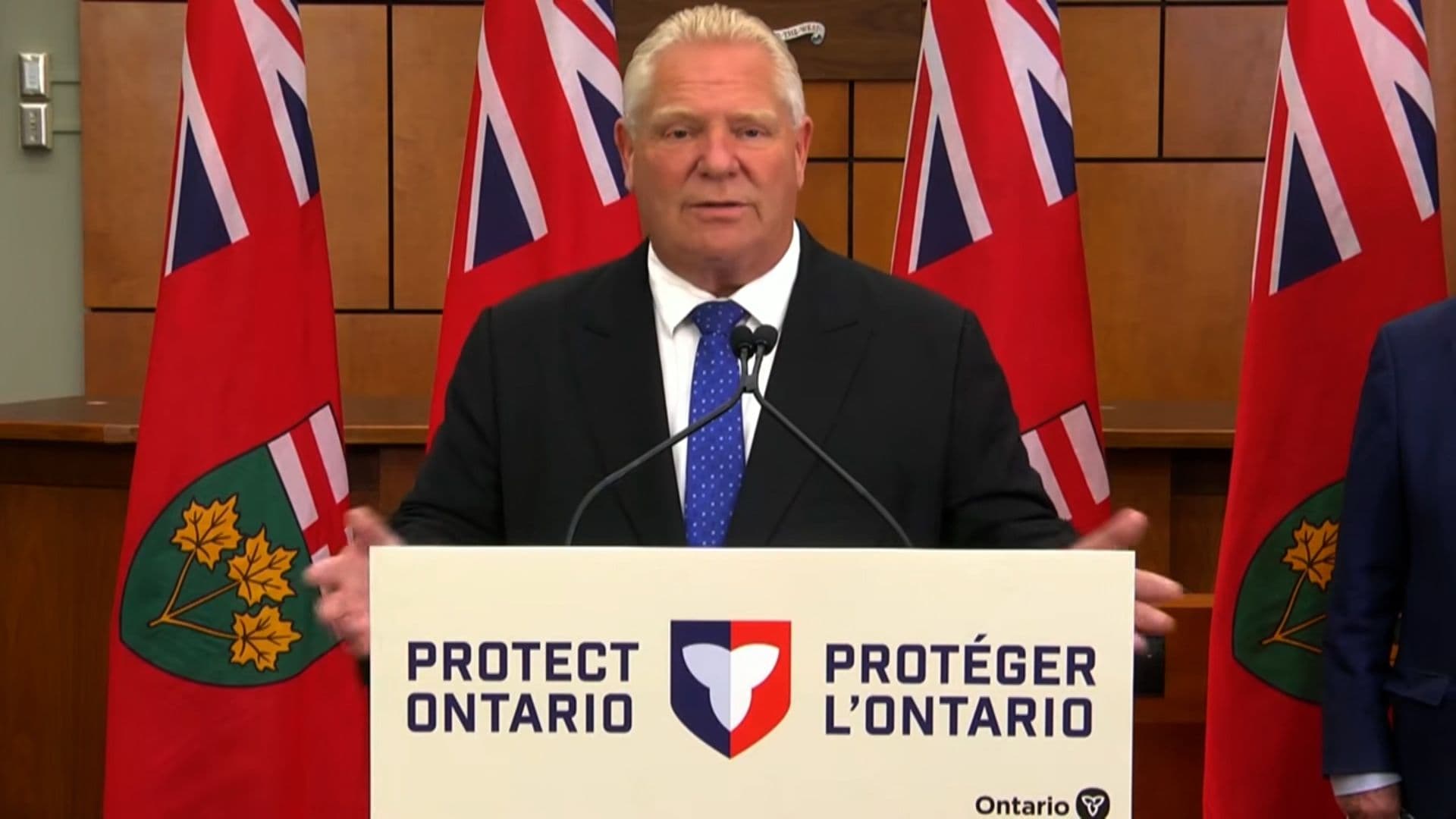 Ontario Premier Doug Ford speaking at a podium with a 'Protect Ontario' sign, representing new alcohol tax policies