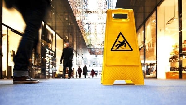Panneau jaune de sol glissant dans un supermarché, symbolisant les dangers cachés ou la vigilance nécessaire.