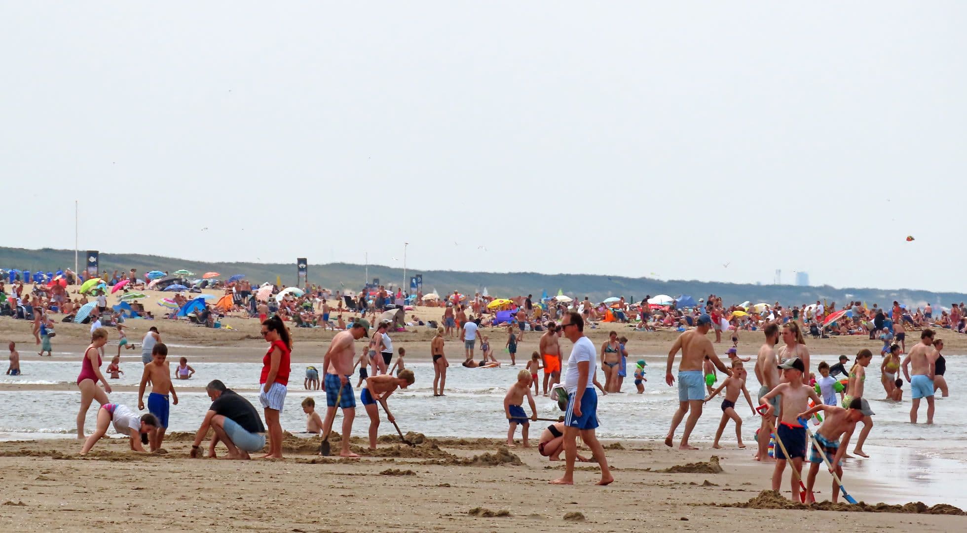 People enjoying a crowded beach under an overcast August sky, reflecting the unpredictable nature of summer's end.