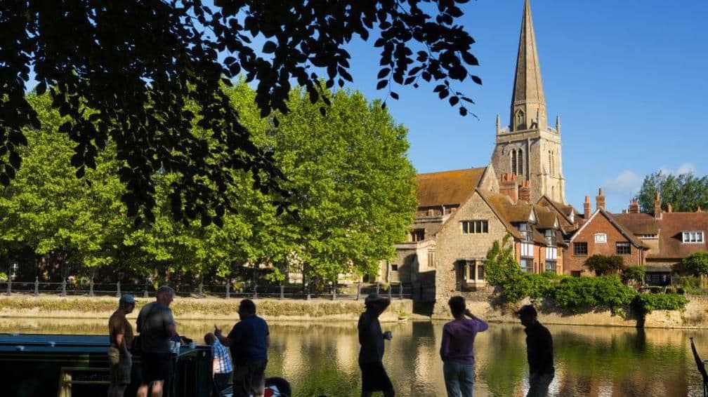 People enjoying a sunny day by a British river, reflecting the public's hope for continued warm weather in August.