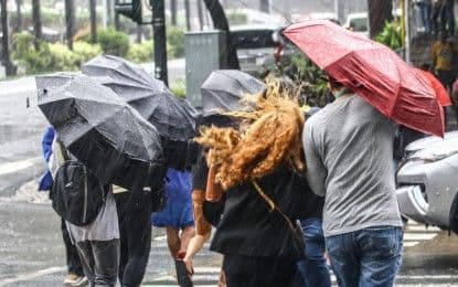 People holding umbrellas struggling against heavy rain and wind, depicting the daily impact of weather conditions like scattered rain showers.