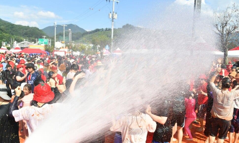 People in Korea getting sprayed with water during a summer festival to escape extreme heat, symbolizing the dual challenge of sweat and storms.