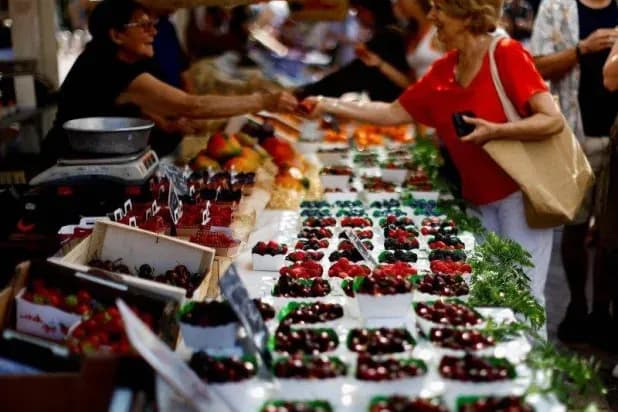 People shopping for fresh produce at a market, illustrating the impact of rising debt costs on household budgets and consumer prices.