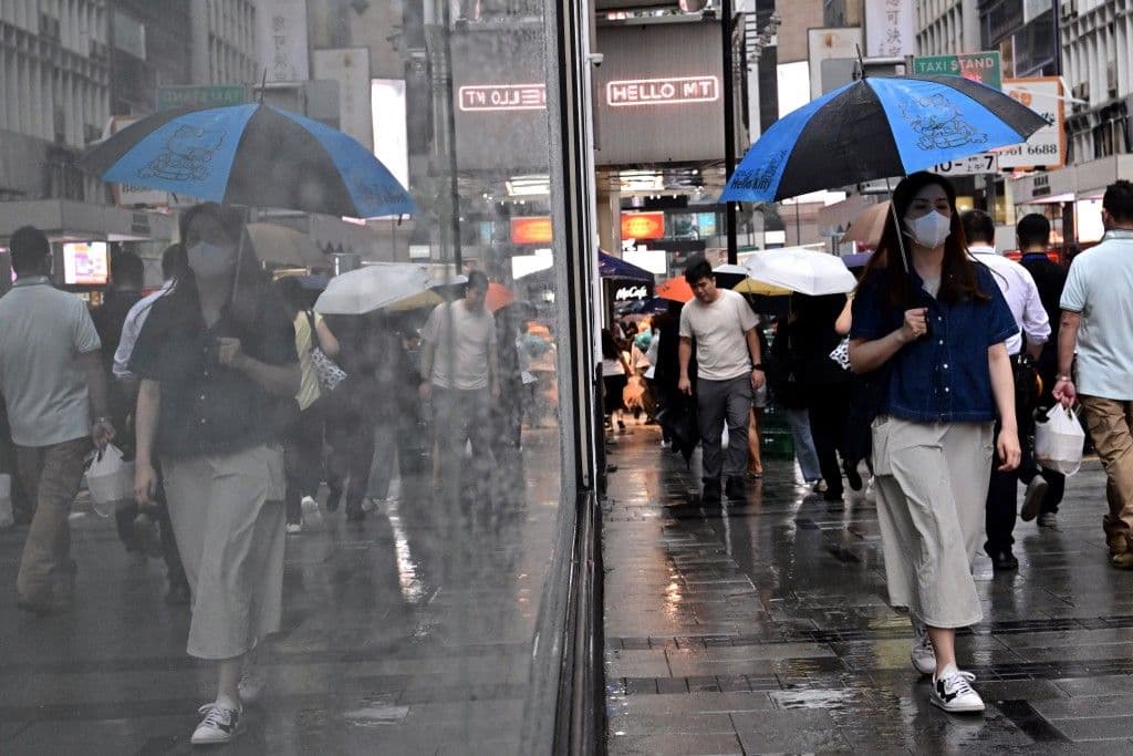 People walk with umbrellas on a rainy street in a bustling city, demonstrating daily life continuing amidst challenging weather.